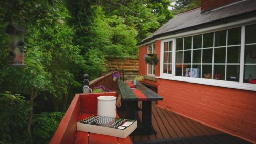 a red house with a bench on a deck at River Cottage at Old Post Office in Bardon Mill