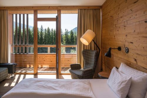a bedroom with a bed and a chair and a window at Falkensteiner Hotel Schladming l 4 Star Superior in Schladming