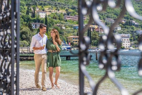 a man and a woman walking on a beach at Hotel Val Di Sogno - Adults Only in Malcesine