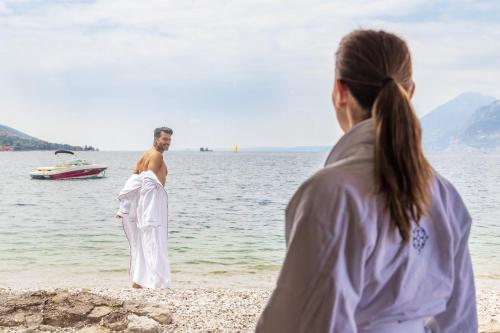 a man and woman standing on a beach near the water at Hotel Val Di Sogno - Adults Only in Malcesine