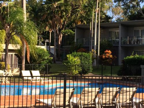 un complexe avec une piscine bordée de chaises et de palmiers dans l'établissement Arcadia Village Motel, à Arcadia