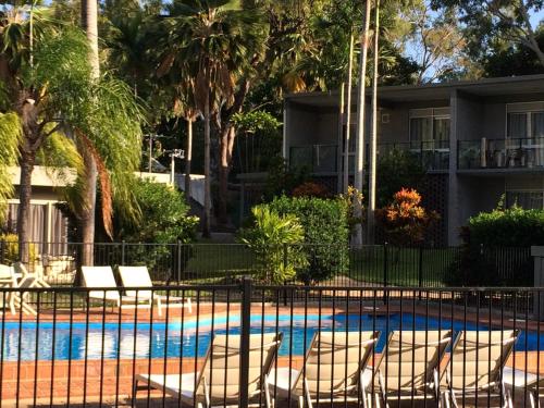 a resort with a pool with chairs and palm trees at Arcadia Village Motel in Arcadia