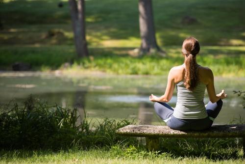 a woman sitting on a bench doing yoga by a pond at The Mayflower Inn & Spa, Auberge Collection in Washington