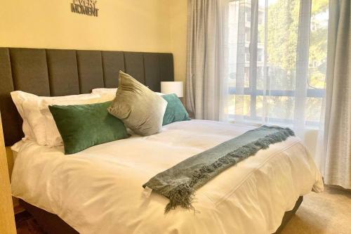 a bed with green and white pillows and a window at Phoenix Rising Apartment in Midrand