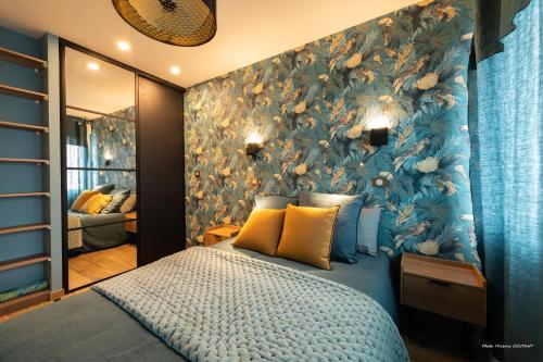 1 dormitorio con cama azul y papel pintado con motivos florales en Le Marchand De Sable - Maisonnette climatisée classée 4 étoiles - 2 Personnes - Plage de la Grande Conche à 200m - ROYAN en Royan