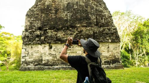 a person taking a picture of a building with a camera at Jungle Lodge Tikal Hostal in Tikal