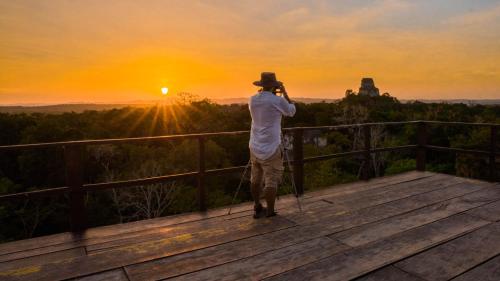 
a man standing on a ledge looking out at the ocean at Hotel Jungle Lodge Tikal in Tikal
