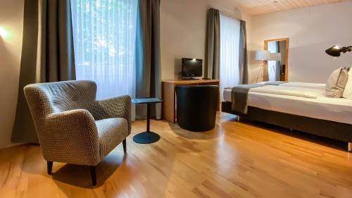 ein Schlafzimmer mit einem Bett, einem Stuhl und einem TV in der Unterkunft IMPULSIV Hotel & Sportresort in Lörrach