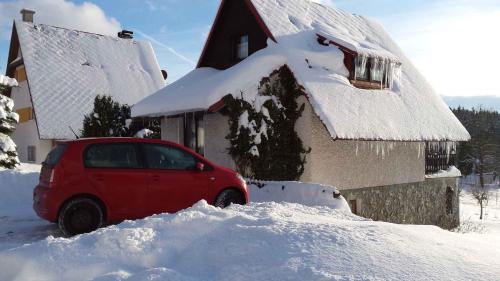 a red car parked in front of a house covered in snow at Holiday home Marianska - Erzgebirge 1668 in Mariánská
