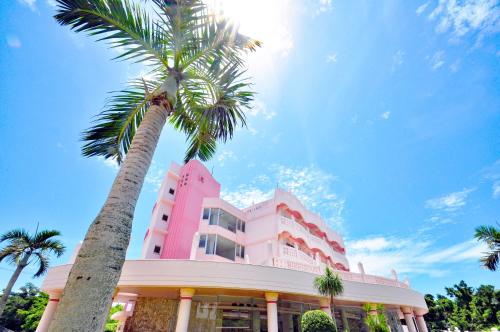 a pink building with a palm tree in front of it at Marine Lodge Marea in Miyako-jima