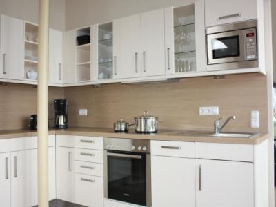 a kitchen with white cabinets and a sink and a microwave at BadeWerk Appartements in Neuharlingersiel