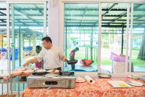 a man cooking food on a stove in a kitchen at หาดตื้น คลื่นสวย รีสอร์ท - Hadtuen Kluensuay Resort in Chao Lao Beach