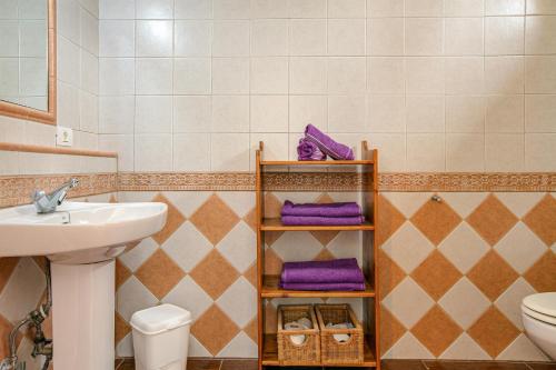 a bathroom with a sink and a toilet and purple towels at Holiday Cottage Santa Lucía in Santa Lucía