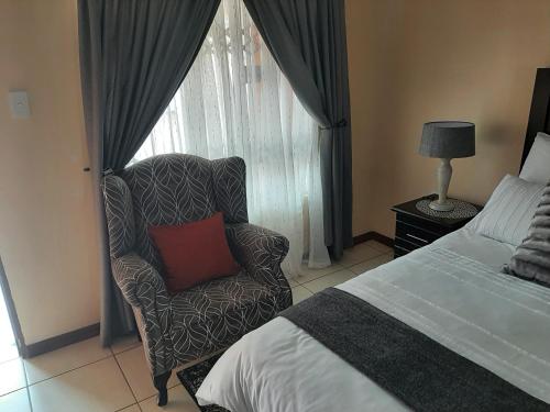 um quarto com uma cadeira, uma cama e uma janela em Lesedi Self Catering em Pretoria