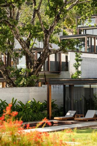 a house with two lounge chairs in front of a tree at The Naka Phuket, a member of Design Hotels in Kamala Beach