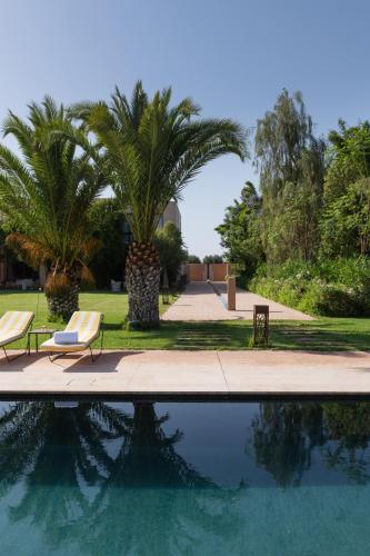 a swimming pool with two chairs and a palm tree at Pavillon Terra Ababila en Exclusivité in Marrakech
