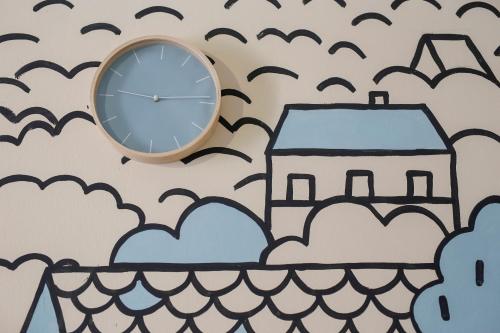 a clock on a wall with a house and clouds at Uránia Apartmanház in Eger
