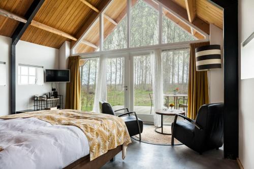 a bedroom with a bed and chairs and a large window at B&B Grevenberg in Oosterhesselen