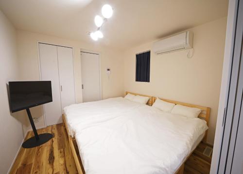 um quarto com uma cama branca e uma televisão de ecrã plano em スポルト東京 em Tóquio