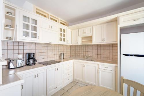 a white kitchen with white cabinets and a refrigerator at Golden Grey Goose in Fira