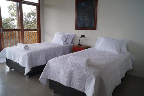 two beds with white sheets in a room with a window at Indano Art Lodge in Lamas