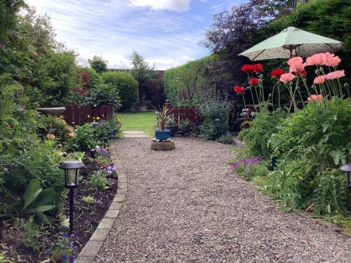 a garden with a pathway with flowers and an umbrella at The Garden Flat in Crieff