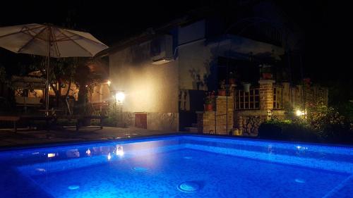 a swimming pool at night with an umbrella at СПА къща за гости Каза Роза - Swiss Style Chalet Casa Rosa SPA Guest House in Kyustendil