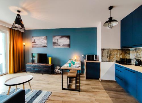 a kitchen and living room with blue cabinets and a table at SUNRISE HOME APARTMENTS - LIGHTHOUSE in Gdańsk