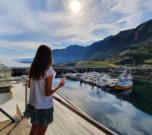 Una bambina che sta su un molo a guardare le barche nell'acqua. di Lofoten Seaside a Ballstad