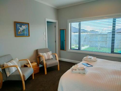 a bedroom with a bed and two chairs and a window at Stay Taupo in Taupo