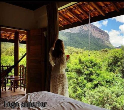 a woman looking out of a window at a mountain at Pousada Rosa dos Ventos Capão in Vale do Capao