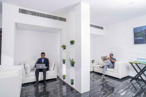 two men sitting on couches in a living room with a laptop at Club Central in Bolpur