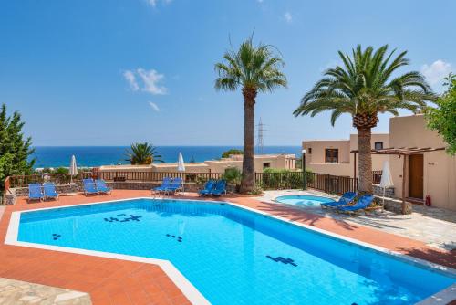 a swimming pool with palm trees and the ocean at Magia Village Resort in Hersonissos