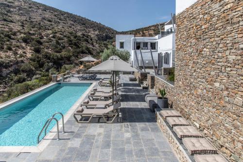 a pool with chairs and umbrellas next to a building at Nesea Sifnos - Luxury Residences in Platis Yialos Sifnos