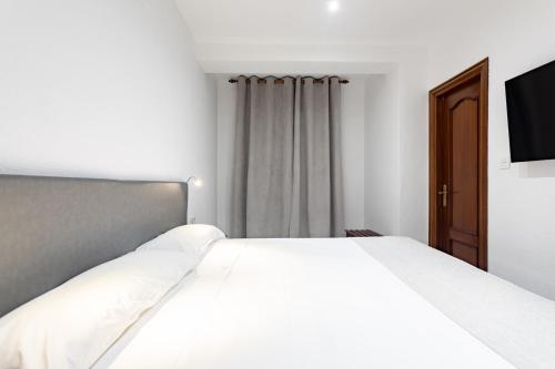 a bedroom with a white bed and a television at Hostal La Costa in El Ejido