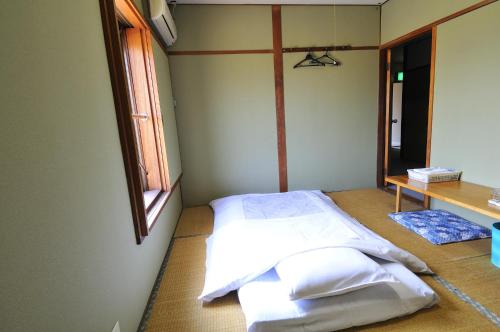 Habitación con cama con sábanas blancas y ventana. en ビジネスホテル六号, en Omitama