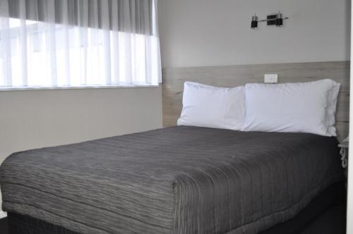 a bed with white pillows and a window in a room at Carramar Motor Inn in Palmerston North