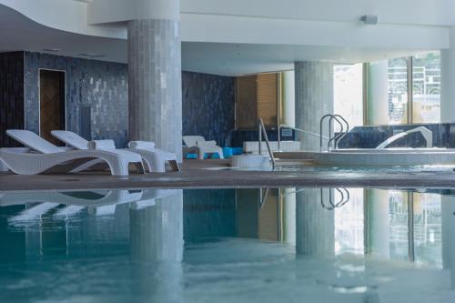 a swimming pool with white chairs in a building at Enjoy Dead Sea Hotel in Ein Bokek