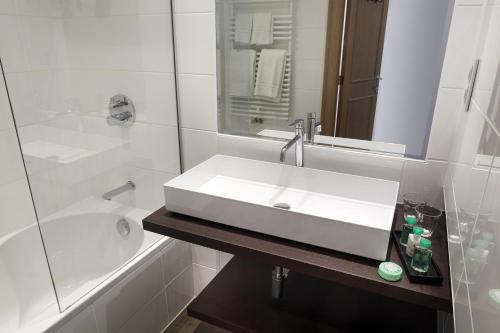 ein weißes Bad mit einem Waschbecken und einer Dusche in der Unterkunft Beach Hotel in De Haan
