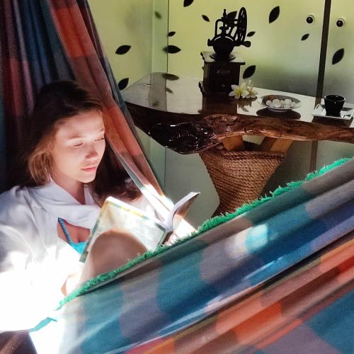 a girl sitting in a hammock reading a book at Pousada Alfa e Ômega in Alto Paraíso de Goiás