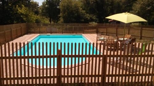 a swimming pool with a fence and an umbrella at les chambres du pont des chèvres in Commensacq