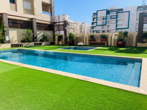 a swimming pool in the middle of a building with green grass at L'APPARTEMENT PARADISIAQUE A HAMMAMET ET NABEUL in Nabeul