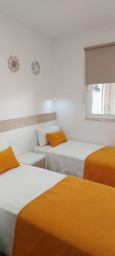 Habitación con 3 camas con sábanas de color naranja y ventana en CASA BIA, en Portimão