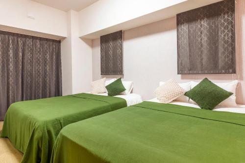 two beds in a room with green sheets at Rizo Zaizen Hotel in Ginowan
