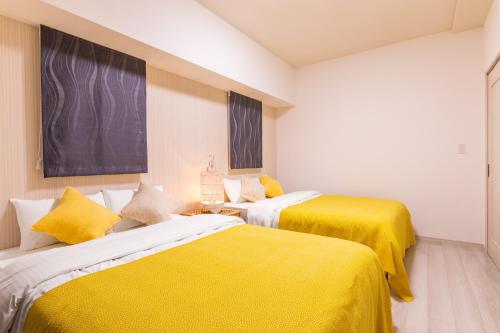 two beds in a room with yellow sheets at Rizo Zaizen Hotel in Ginowan