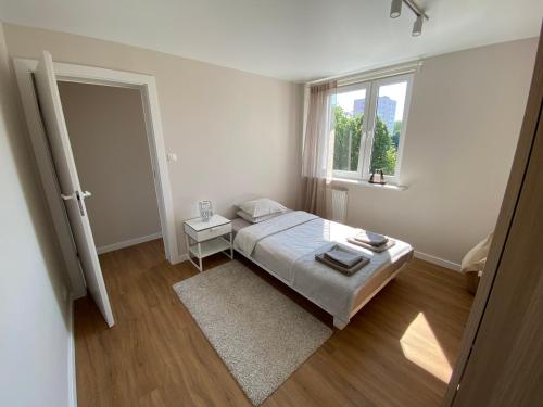a white bedroom with a bed and a window at Apartament Narcyzowa in Gdynia