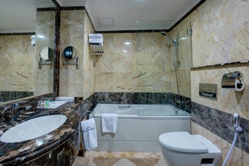 a bathroom with a tub and a toilet and a sink at Sharjah Palace Hotel in Sharjah