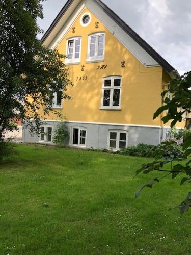 une grande maison jaune avec une cour devant elle dans l'établissement Allesø Gl. sognefoged gård, à Odense