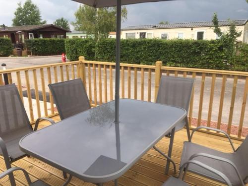 a table and chairs with an umbrella on a deck at Poppy Lodge in High Hesket