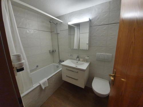 a bathroom with a sink and a toilet and a tub at Aparthotel Ambassador in Bellwald